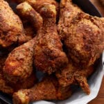 Crispy golden brown gluten-free fried chicken stacked in a paper towel lined black skillet. The skillet is resting on a wooden surface.
