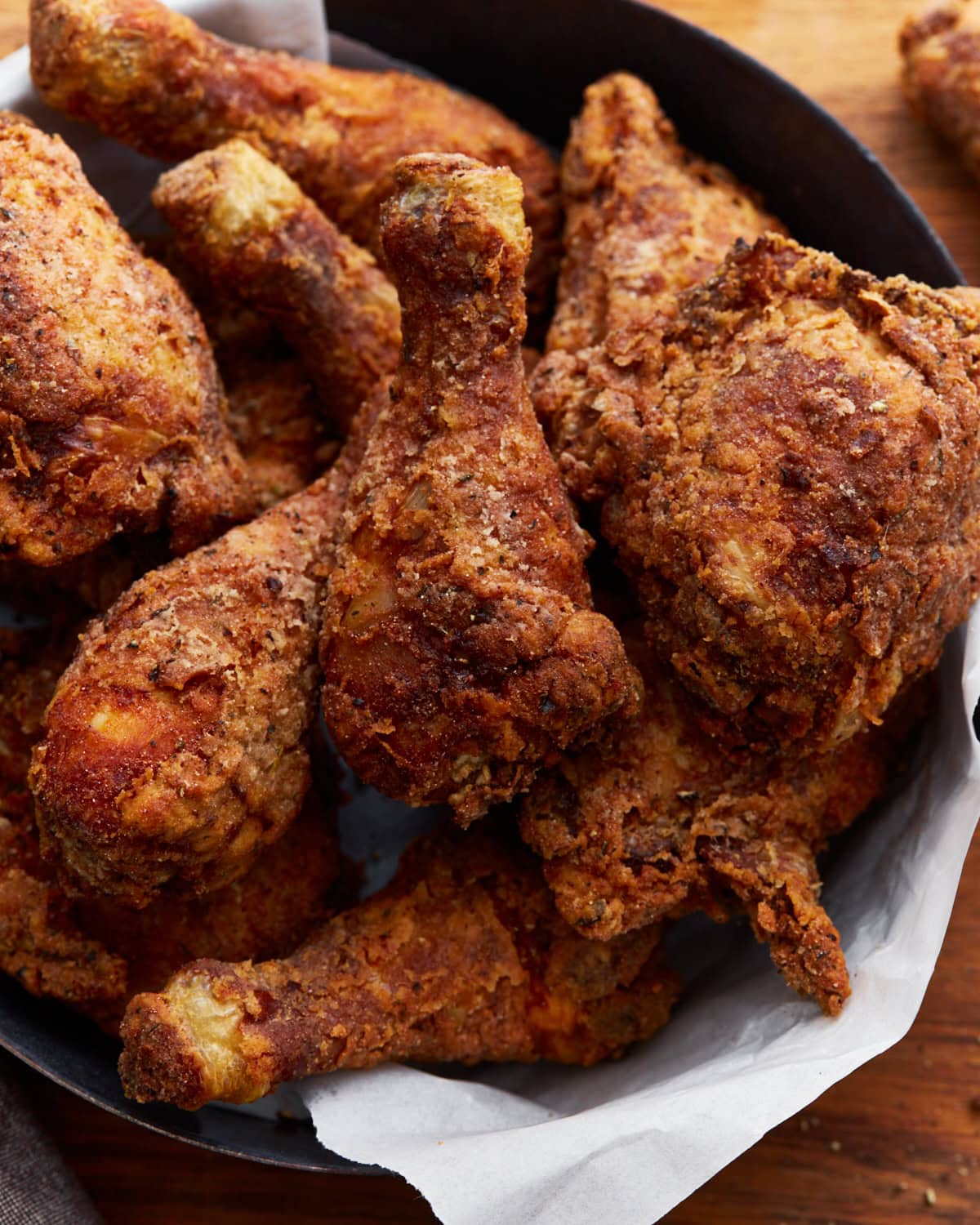 Crispy golden brown gluten-free fried chicken stacked in a paper towel lined black skillet. The skillet is resting on a wooden surface.