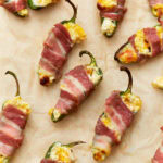 Close-up of bacon-wrapped keto jalapeño poppers stuffed with a creamy cheese mixture, placed on parchment paper, golden and crispy from baking.