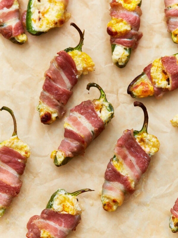 Close-up of bacon-wrapped keto jalapeño poppers stuffed with a creamy cheese mixture, placed on parchment paper, golden and crispy from baking.