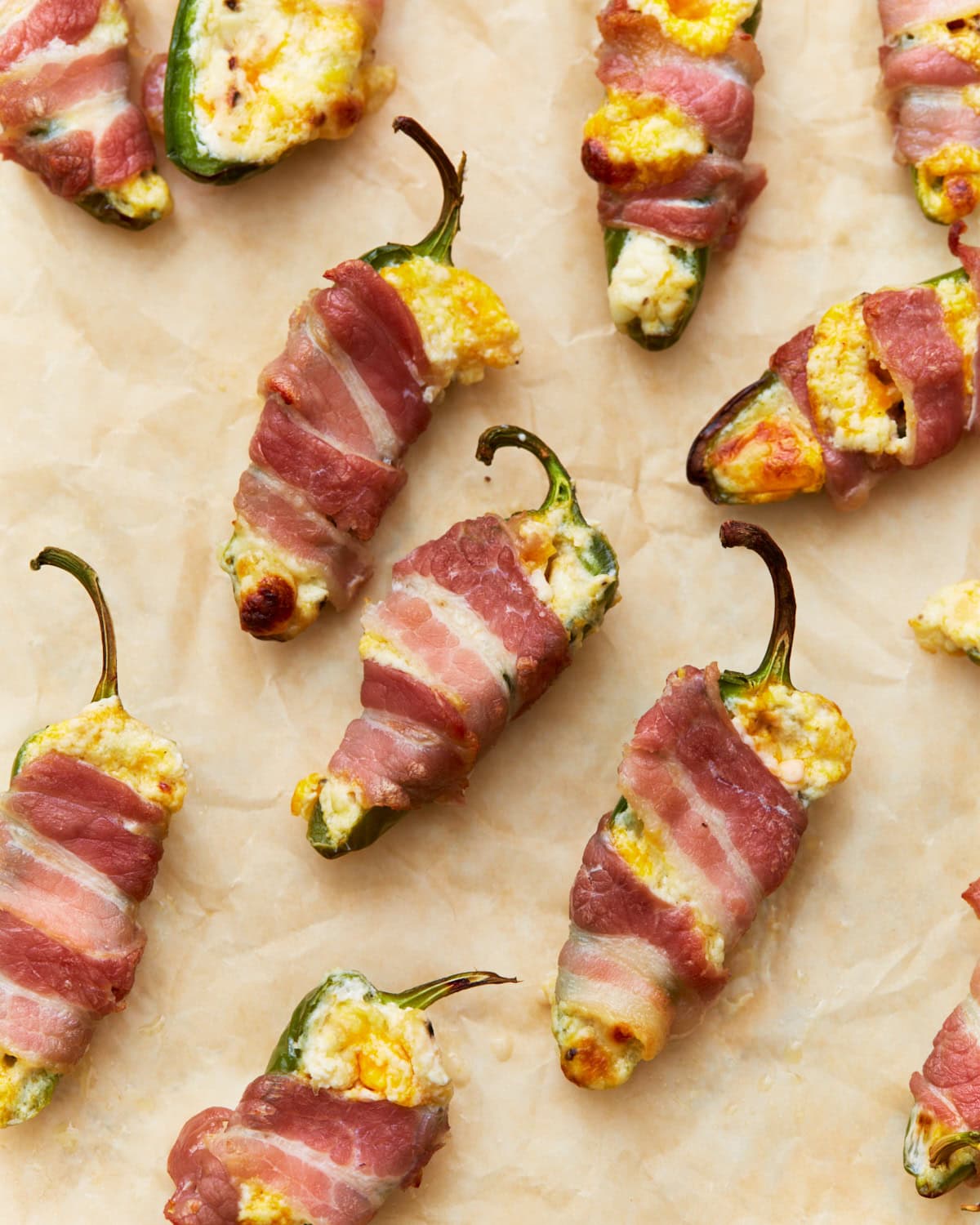 Close-up of bacon-wrapped keto jalapeño poppers stuffed with a creamy cheese mixture, placed on parchment paper, golden and crispy from baking.