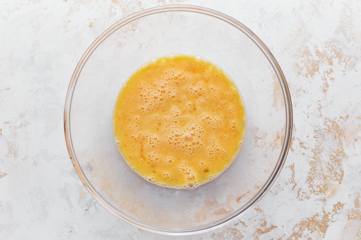 Egg and fresh lemon juice whisked together in a glass mixing bowl resting on a light surface.