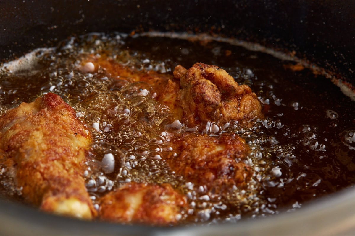 Gluten-free fried chicken frying to golden brown in bubbling frying oil in a cast iron skillet.