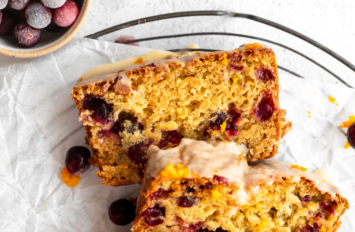 Two slices of gluten free cranberry bread stacked on parchment paper, with a glossy orange glaze drizzled on top.