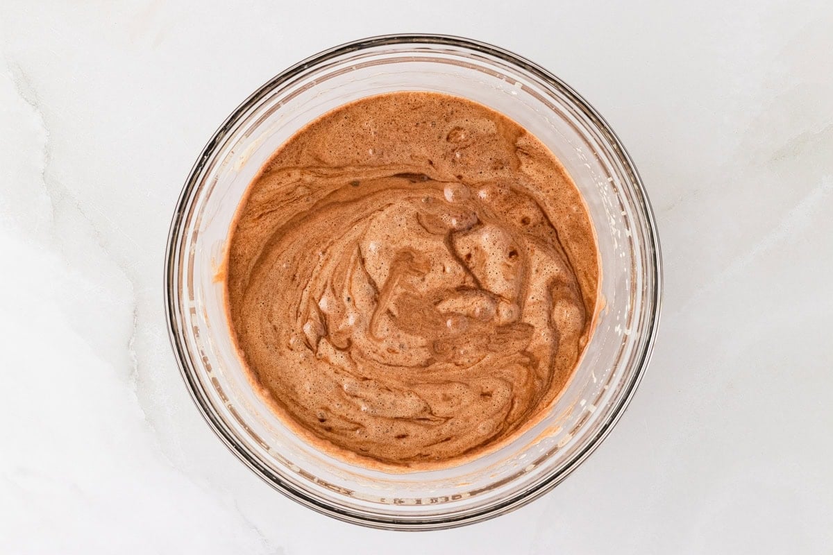 melted chocolate folded into whipped eggs and sugar mixture in a glass bowl