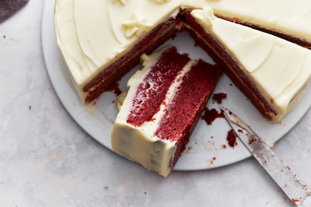 Closeup of gluten-free red velvet cake with cream cheese frosting, decorated with piped flowers, and a slice partially removed