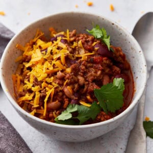 Closeup shot of a white bowl filled with gluten-free chili, topped with parsley and shredded orange cheese.