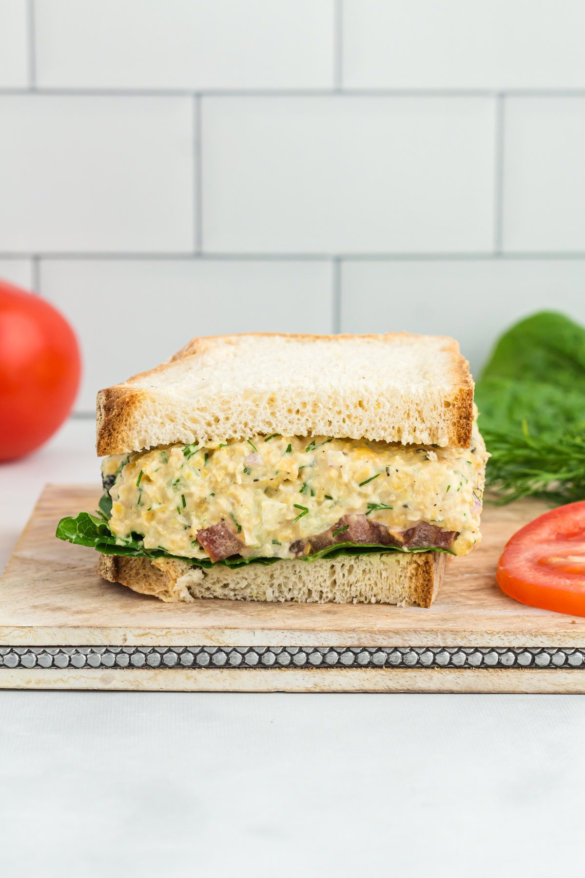 A sandwich made with vegan chickpea tuna salad, featuring creamy filling mixed with herbs and diced vegetables, layered on a slice of bread with fresh greens.