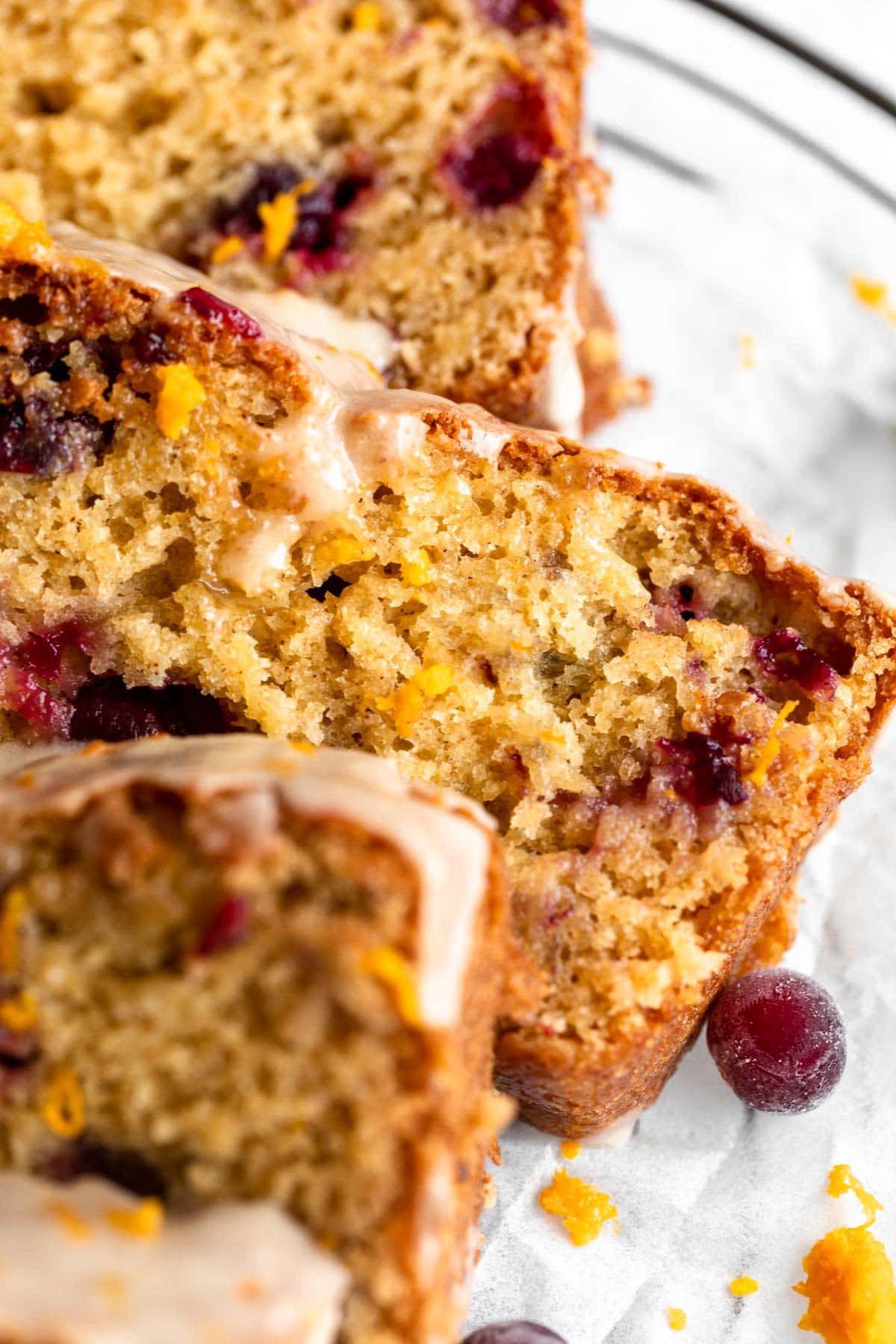 A close up of a few slices of gluten free cranberry bread stacked on a glass plate, with a glossy orange glaze drizzled on top.