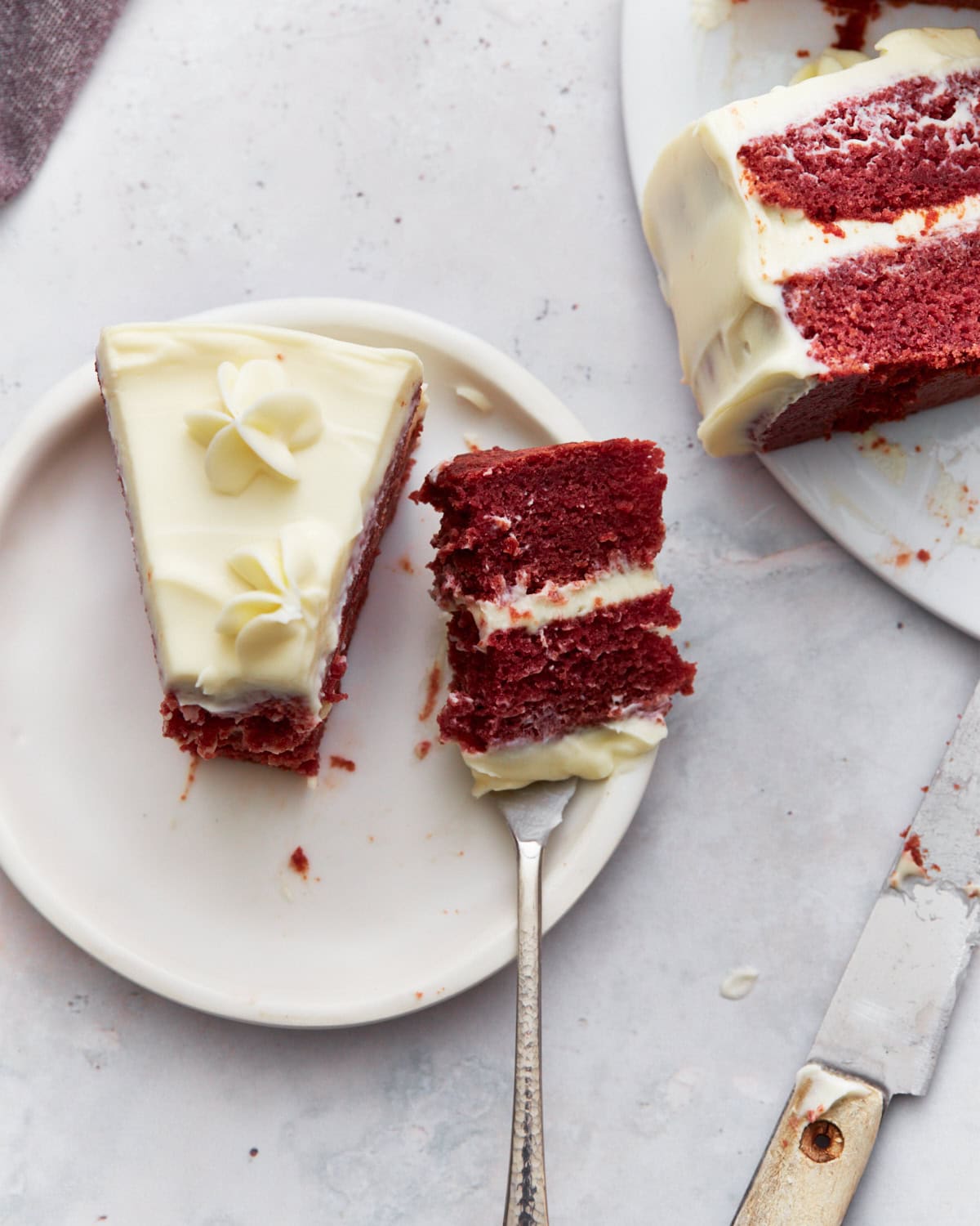 A single slice of gluten-free red velvet cake on a plate, with a fork holding a bite, showing the layers of cream cheese frosting and moist cake.
