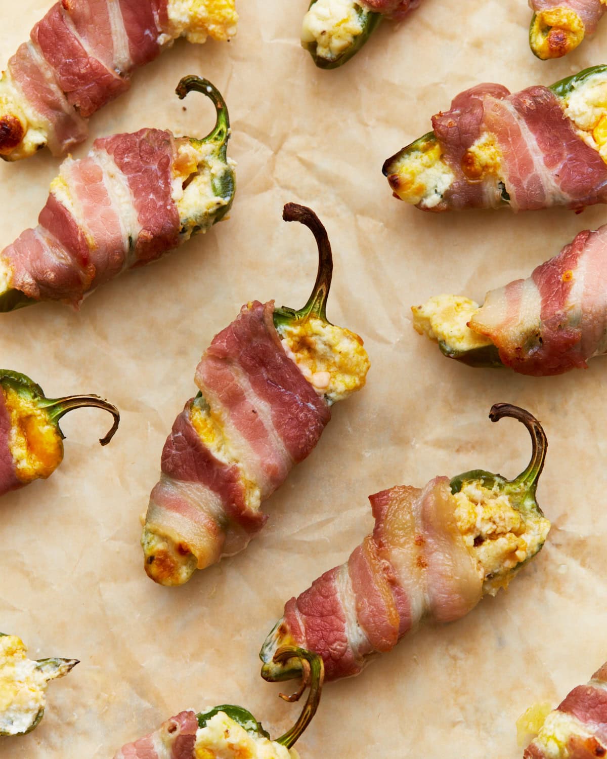 keto jalapeño poppers stuffed with a creamy cheese mixture and wrapped in crispy bacon, placed on parchment paper, golden and crispy from baking.