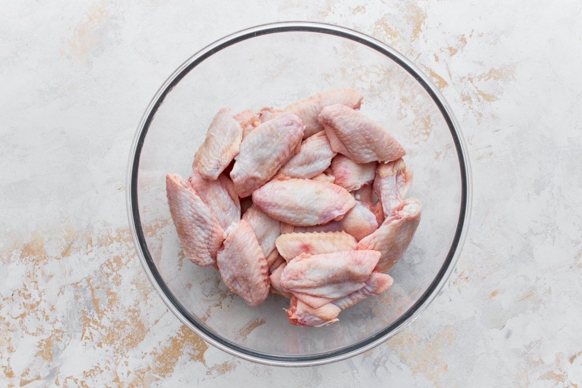 raw chicken wings in a glass bowl on a light colored surface