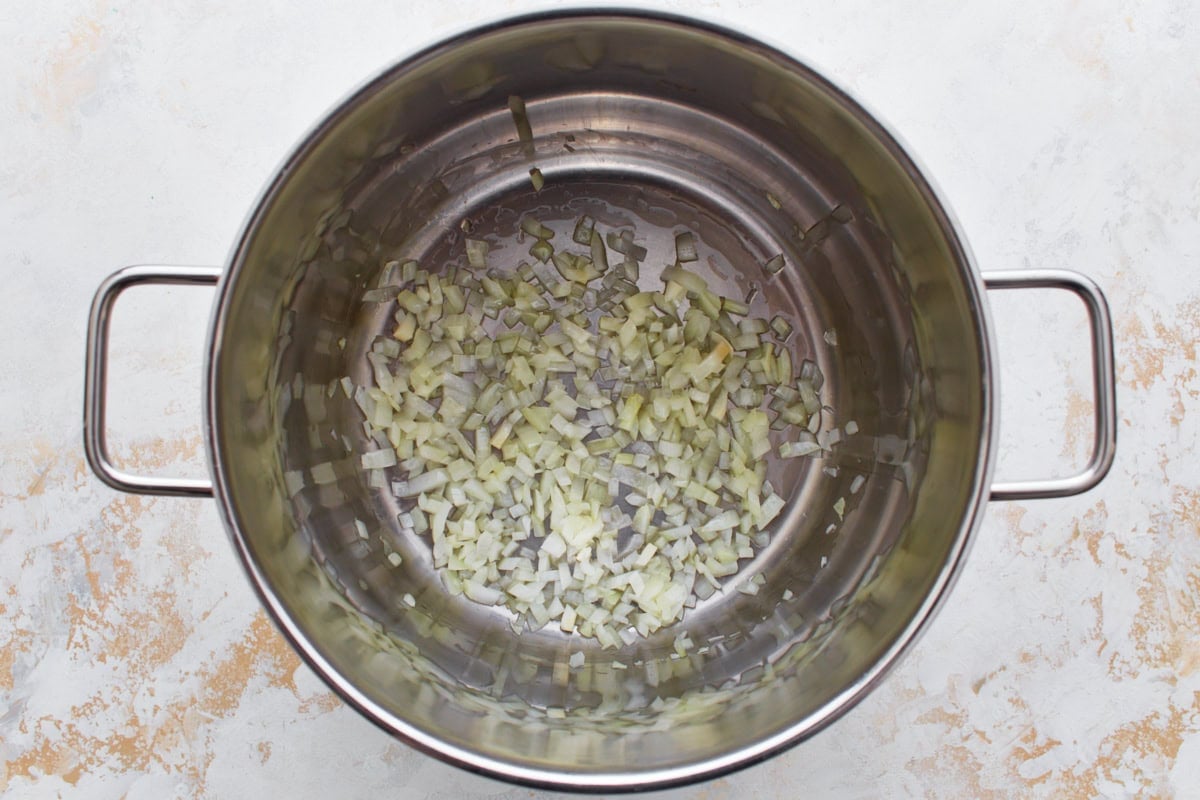 Diced onions sautéing in a large stainless steel pot.