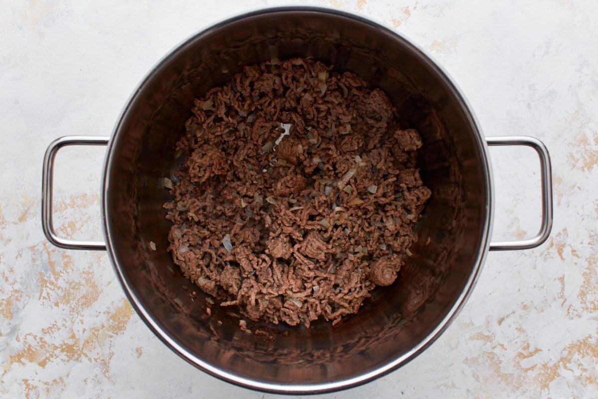 Ground beef crumbled and browning in a large stainless steel pot with died onions