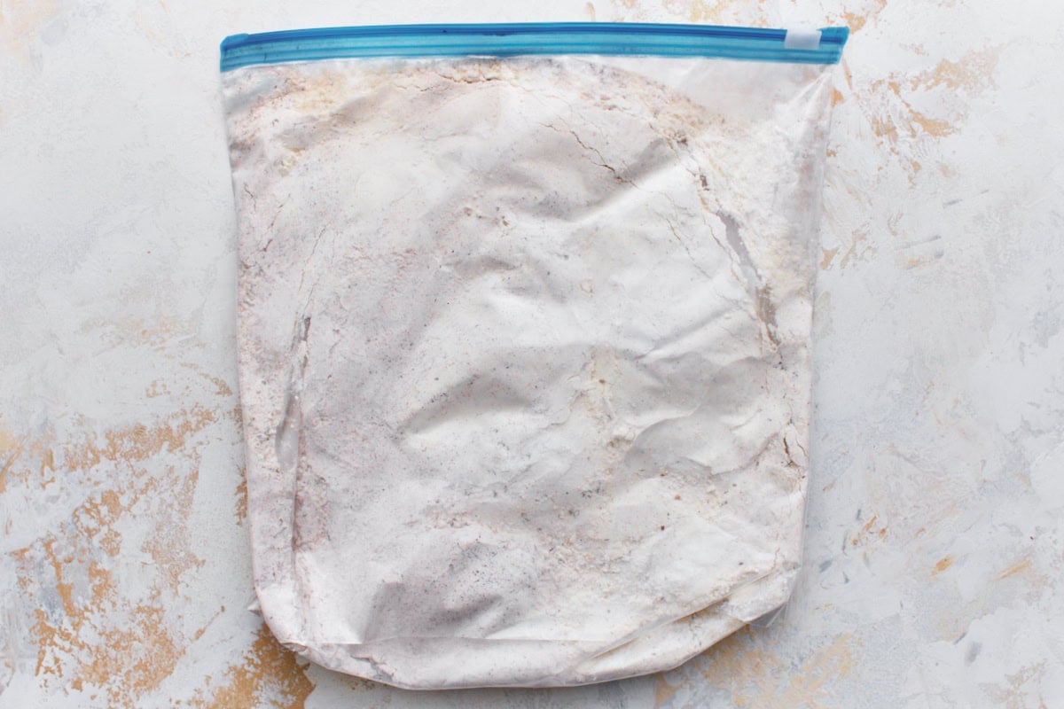 Gluten-free flour, cornstarch, and spice mixture in a large plastic bag laid flat on a light surface.