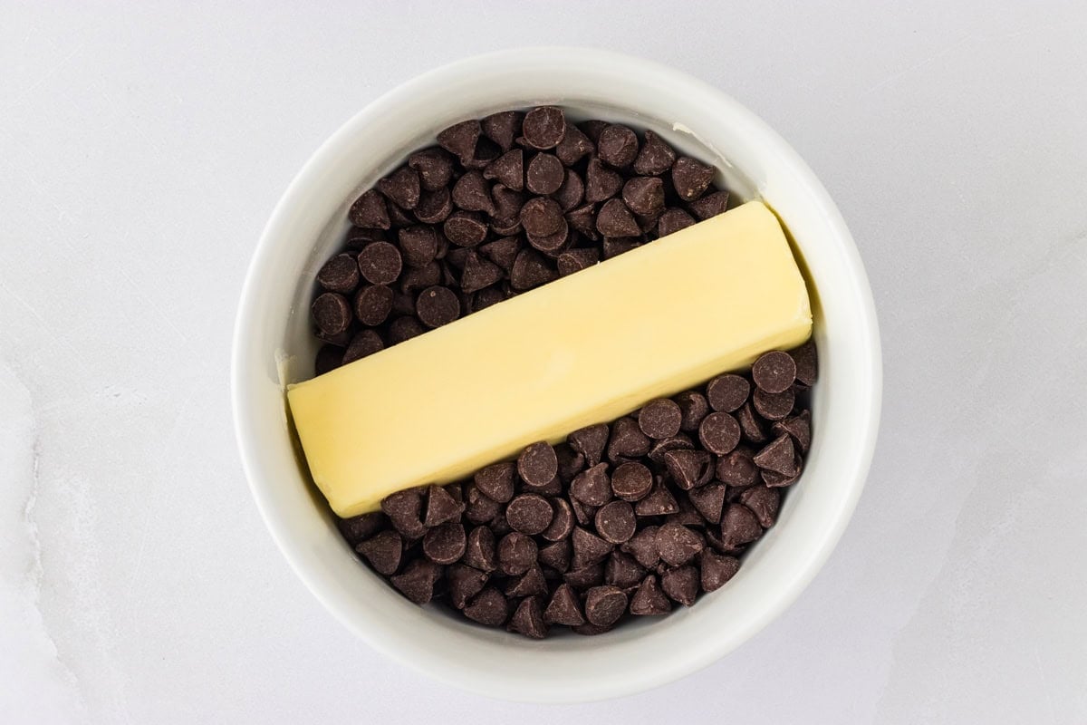 Chocolate chips in a white ramekin with a stick of butter on top.