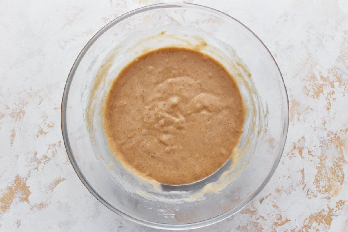 A glass bowl filled with fully mixed gluten-free banana cake batter, placed on a light, textured surface
