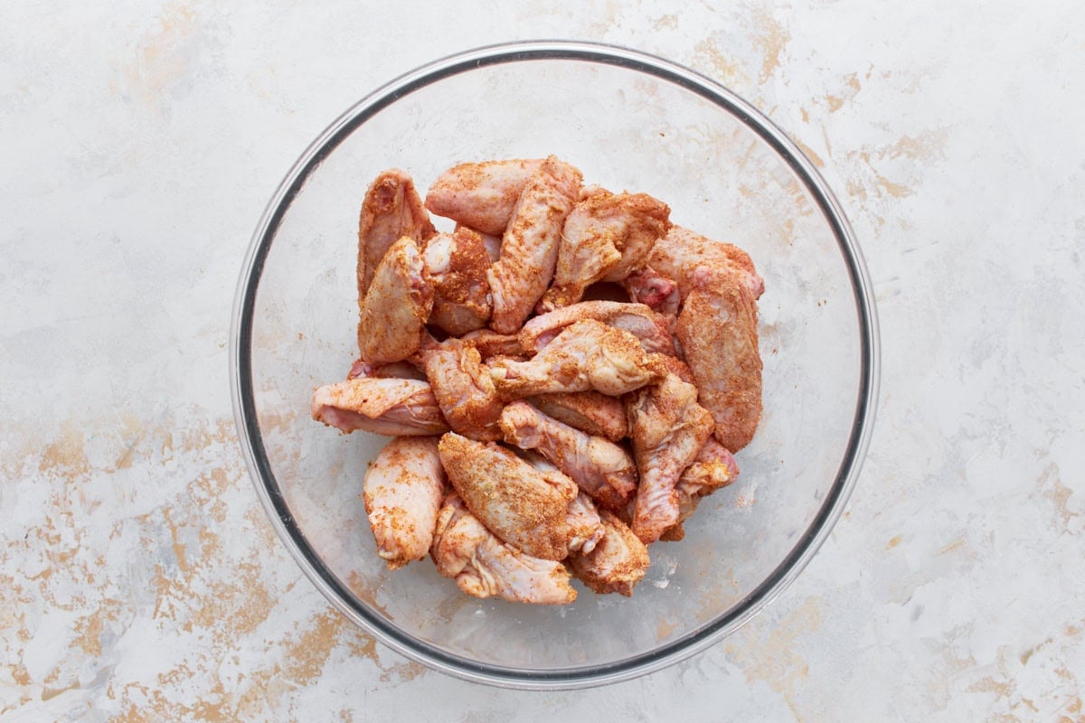 raw chicken wings coated in a dry rub in a glass bowl 