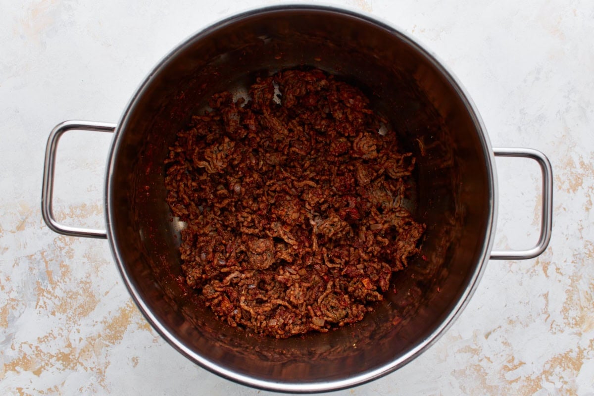 Crumbled and browned ground beef in a large stainless steel pot with died onions and a spice mixture.