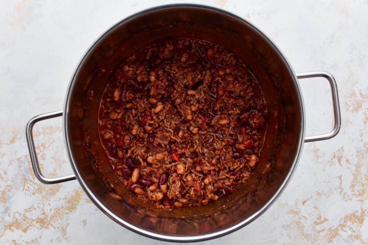 Crumbled and browned ground beef in a large stainless steel pot with died onions, a spice mixture, beans, and tomato sauce