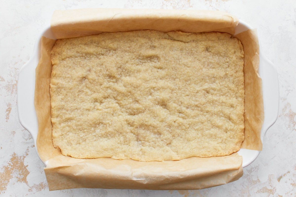 Cooked and slightly browned gluten-free shortbread crust in a parchment paper lined baking dish