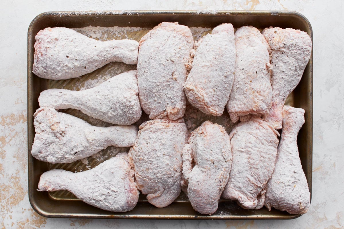 Gluten-free battered chicken thighs and drumsticks lined on a baking sheet