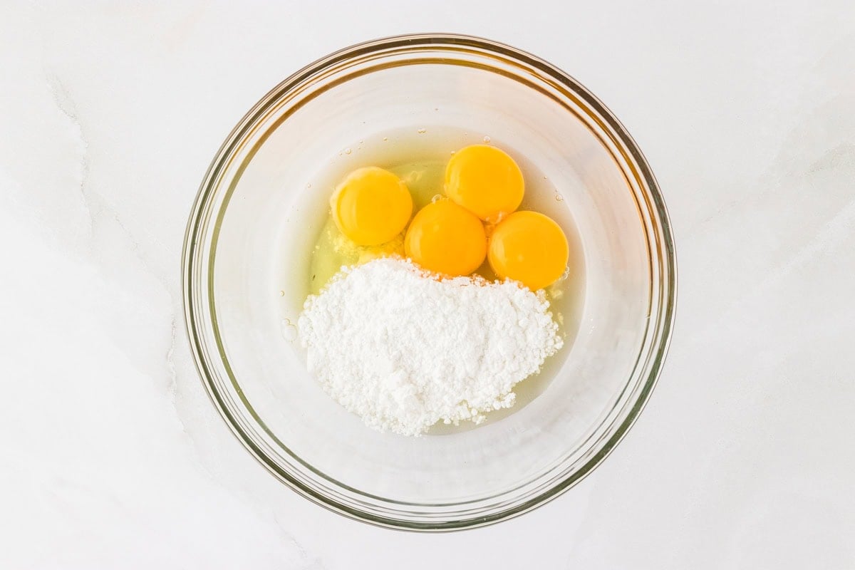 4 egg yolks, eggs whites, and powdered sugar in a glass mixing bowl.