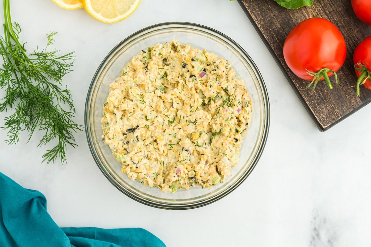 vegan chickpea tuna salad in a large glass bowl with a wooden cutting board in the background 