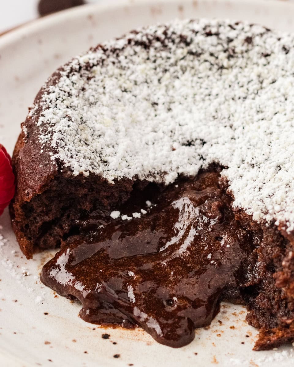 A gluten-free chocolate lava cake on a white plate, dusted with powdered sugar with a gooey chocolate center. 