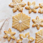 Decorated gluten-free sugar cookies shaped like snowflakes, with white icing on a light textured background.