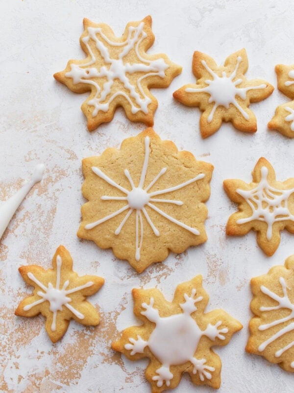 Decorated gluten-free sugar cookies shaped like snowflakes, with white icing on a light textured background.