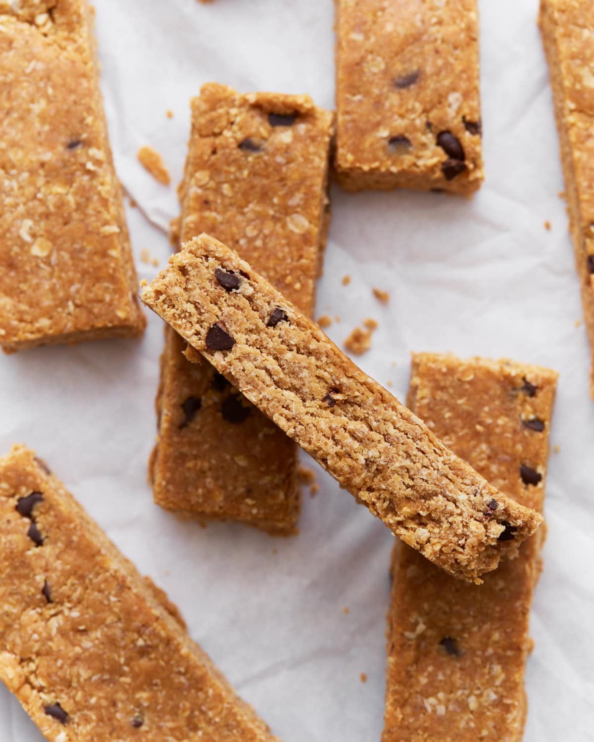 Homemade gluten-free granola bars stacked on parchment paper, showing their golden brown texture and chocolate chip details.