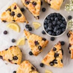 A top-down view of freshly baked gluten-free blueberry scones on parchment paper, drizzled with lemon glaze, surrounded by fresh blueberries and lemon slices.