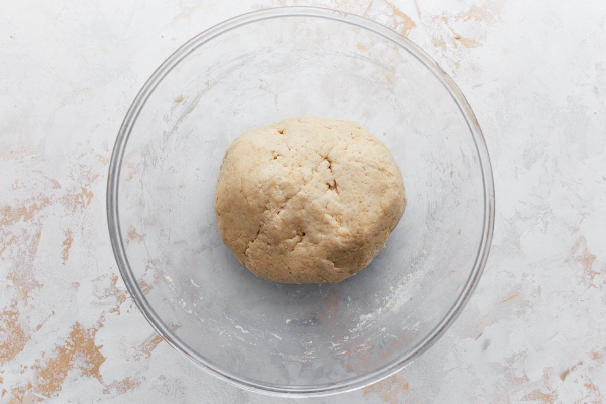A smooth ball of gluten-free naan dough resting in a glass mixing bowl.