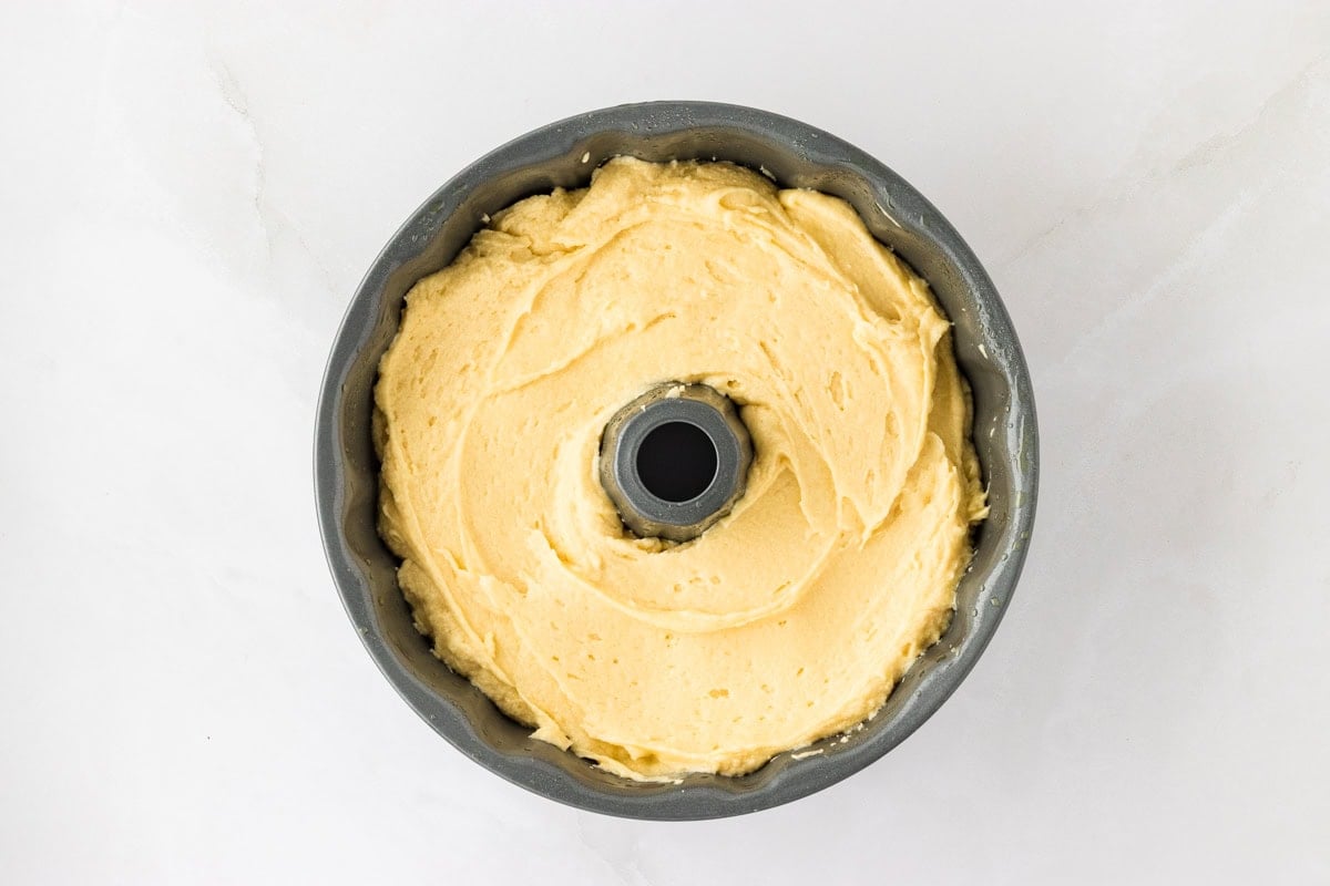 A Bundt pan filled with the prepared gluten-free cake batter, smoothed evenly on top before baking.