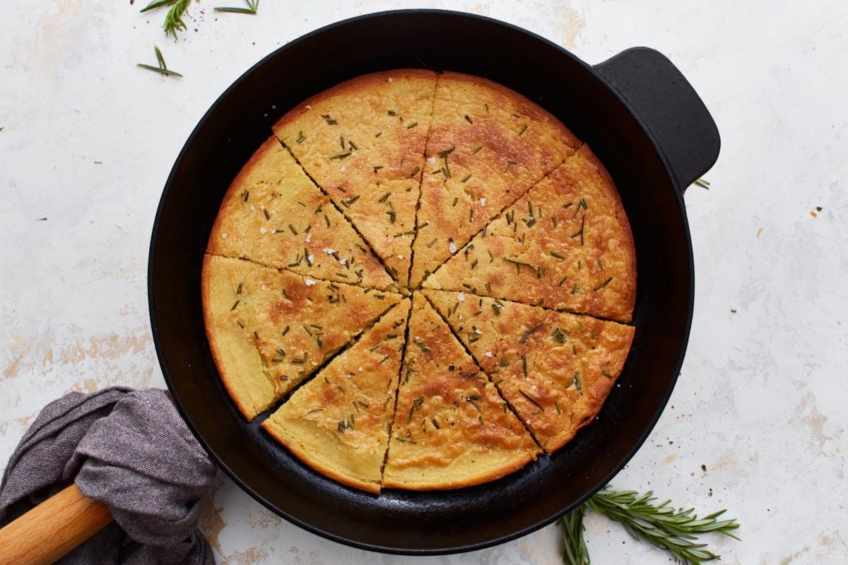 Farinata in a cast iron skillet, sliced and ready to serve, with rosemary sprigs as decoration.