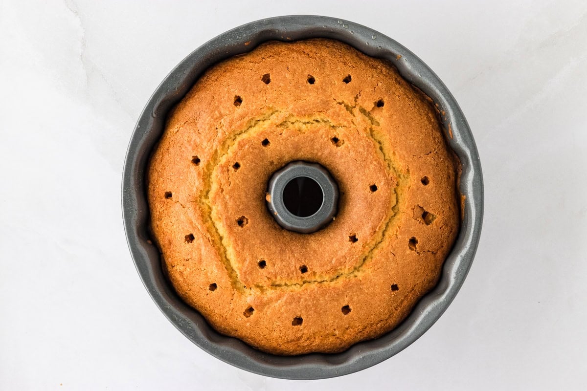 A freshly baked Gluten-Free Kentucky Butter Pound Cake still in the Bundt pan, with holes poked across the surface to allow the glaze to seep in.