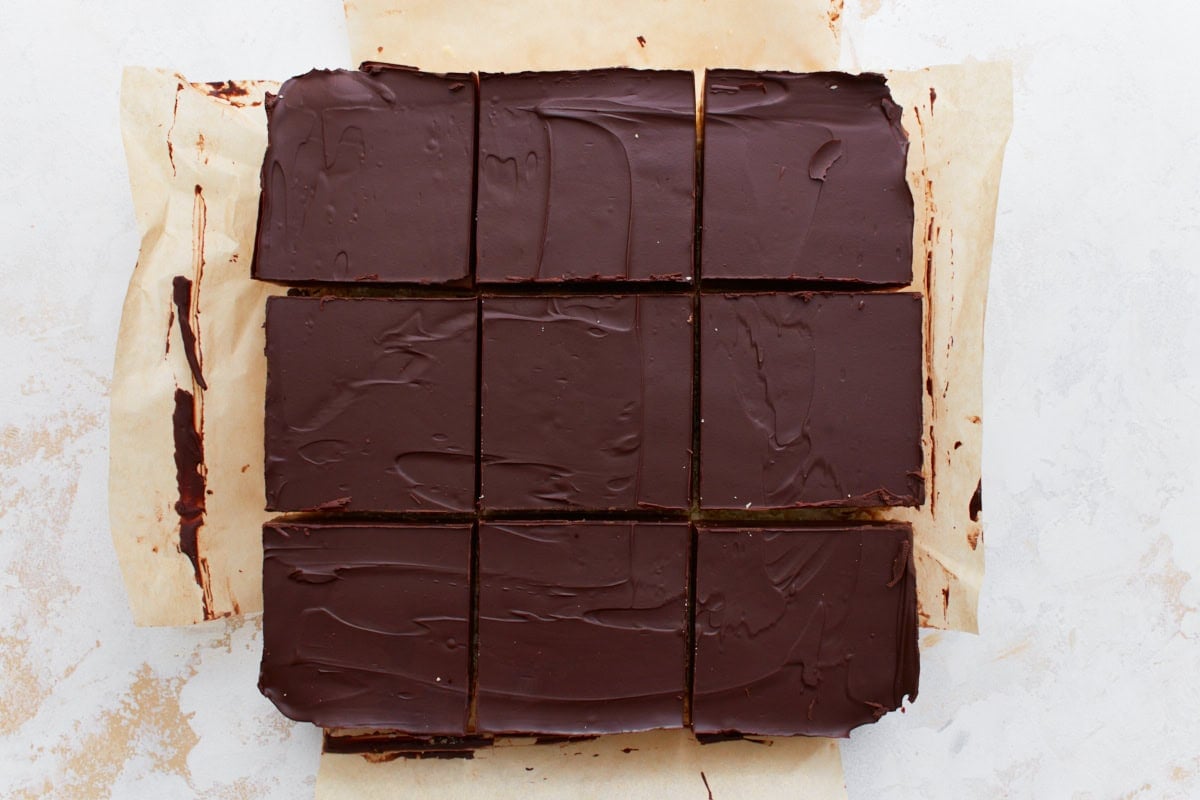 The fully assembled gluten-free millionaire shortbread cut into neat squares on parchment paper, showcasing the chocolate, caramel, and shortbread layers.