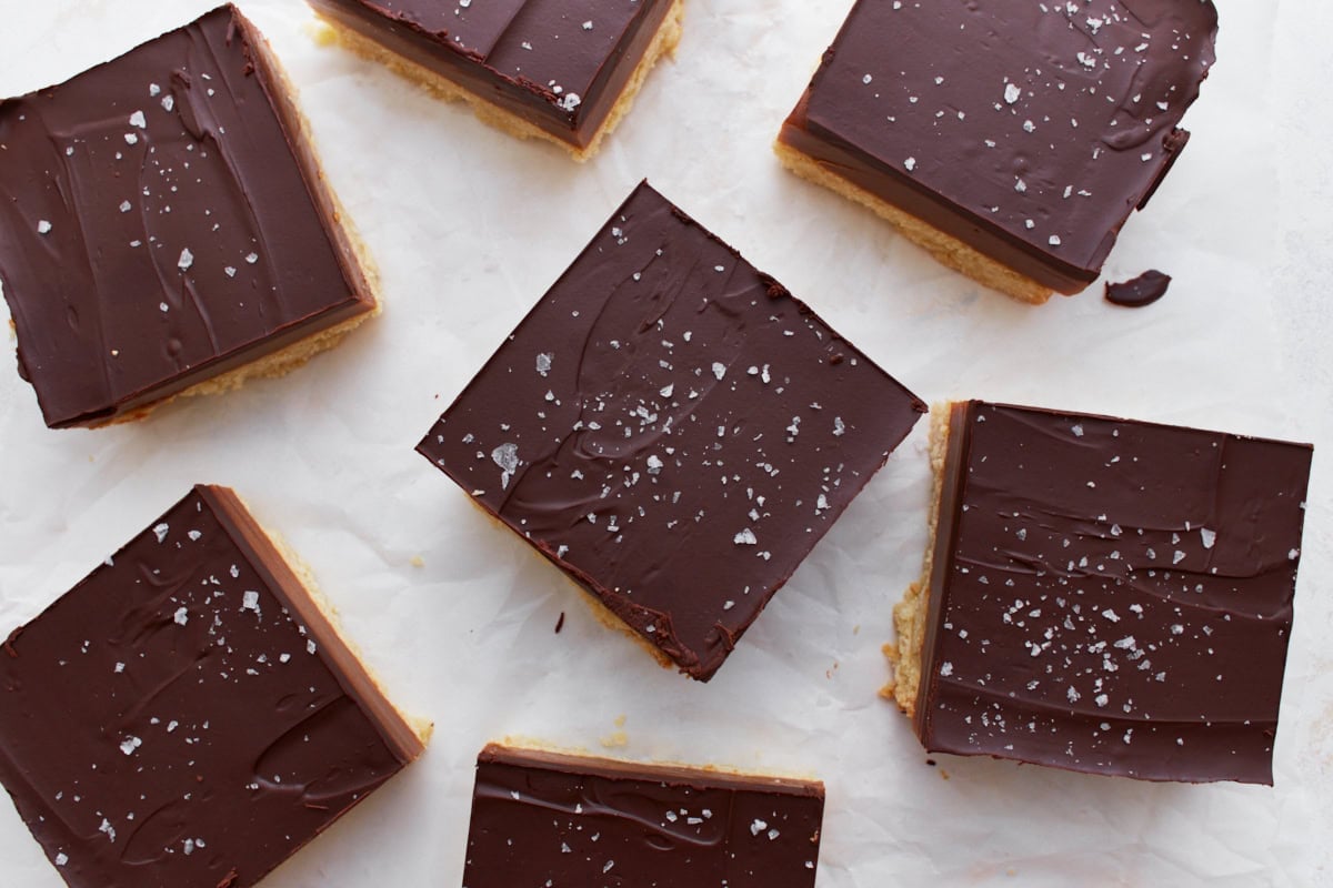 Overhead view of sliced gluten-free millionaire shortbread pieces arranged on parchment paper, each sprinkled with flaky sea salt.