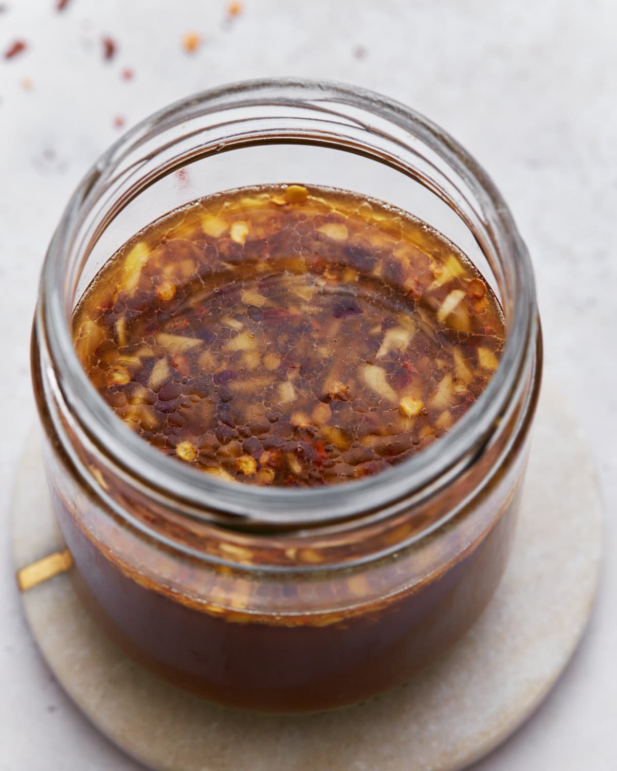 A top-down view of gluten-free stir-fry sauce in a jar, showcasing its rich brown color with garlic and red chili flakes floating on the surface.