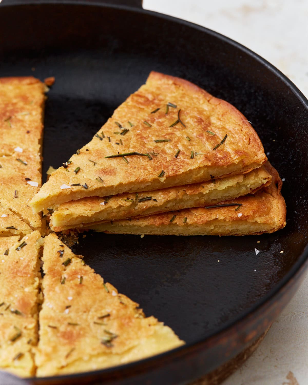 A side view of sliced farinata stacked in a cast iron skillet, showcasing its texture and golden crust.