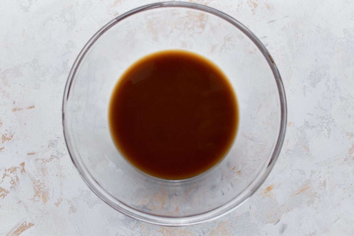 A clear mixing bowl containing a smooth, glossy brown gluten-free stir-fry sauce, ready for use.
