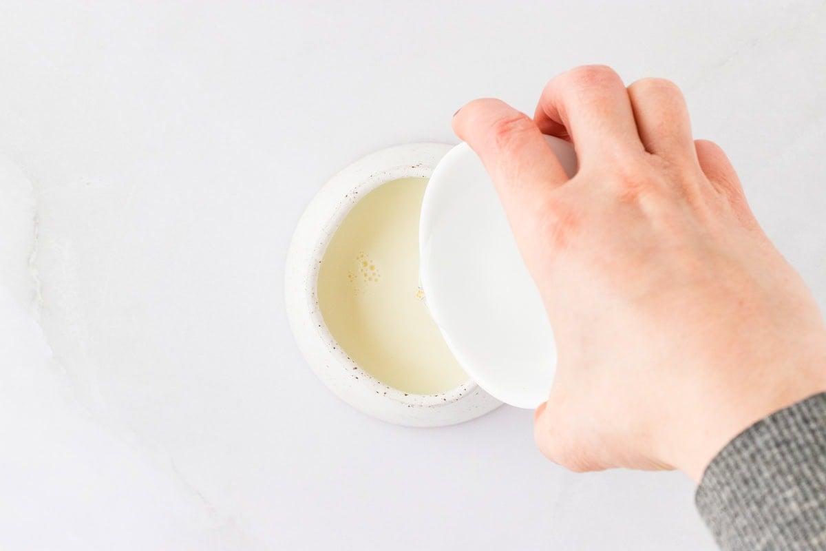 A small bowl of liquid being poured into another bowl, illustrating the preparation of ingredients for the Kentucky Butter Pound Cake.