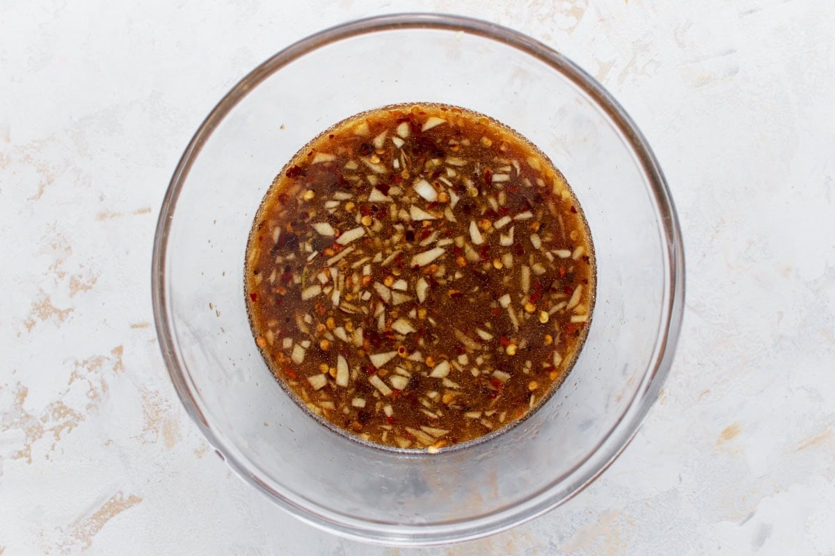A clear mixing bowl of gluten-free stir-fry sauce, showing finely chopped garlic, red chili flakes, and a rich texture that enhances its appearance.