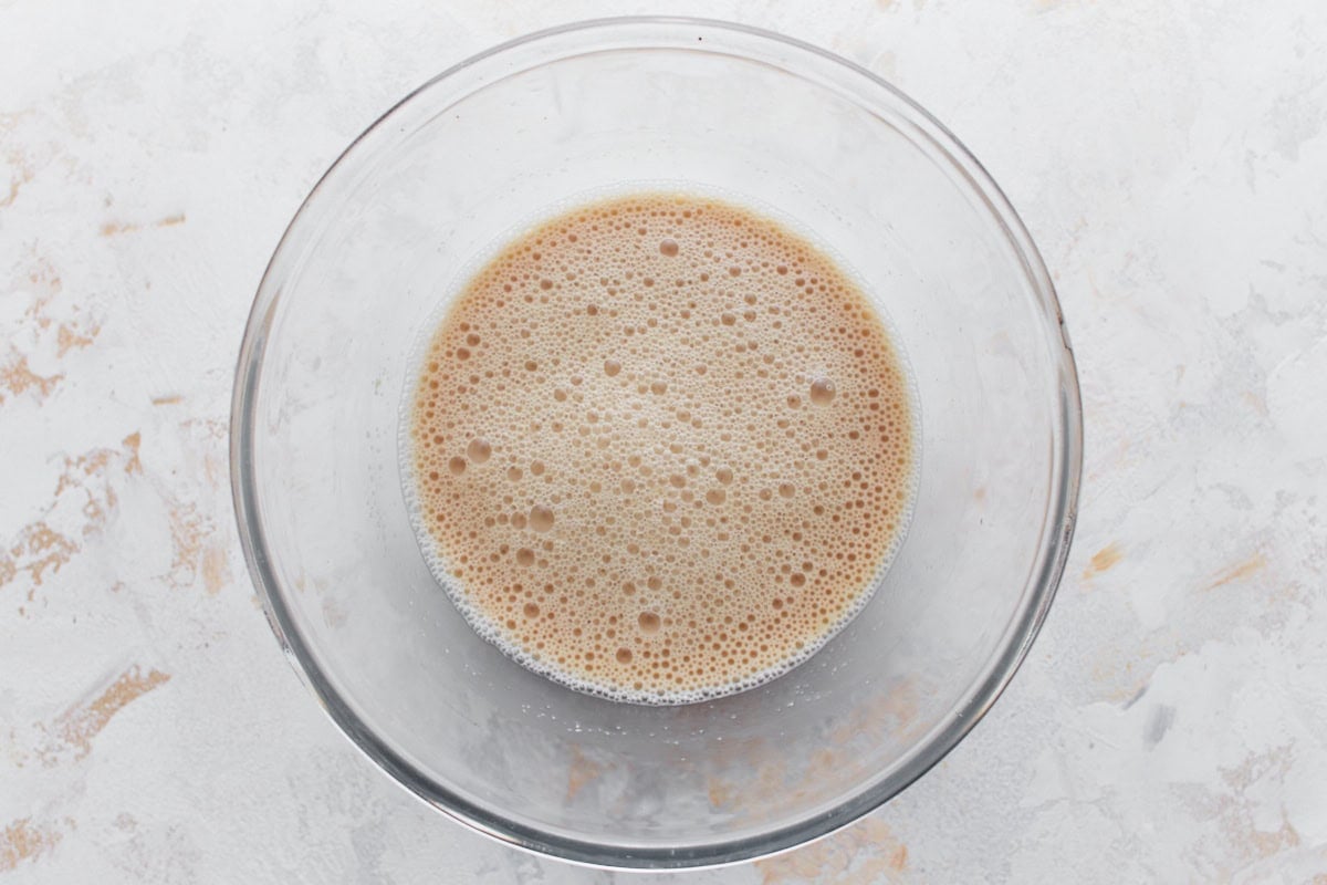 A glass bowl filled with frothy activated yeast mixture.
