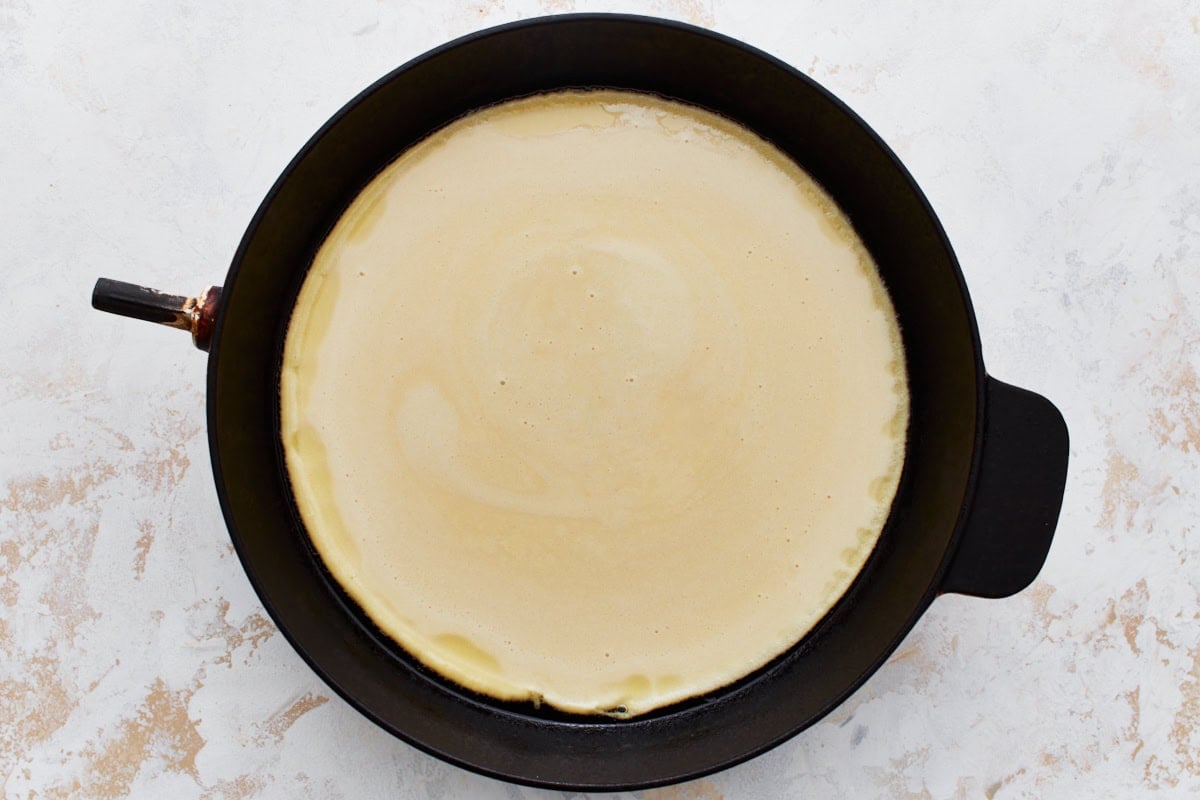 A cast iron skillet filled with uncooked chickpea flour batter.