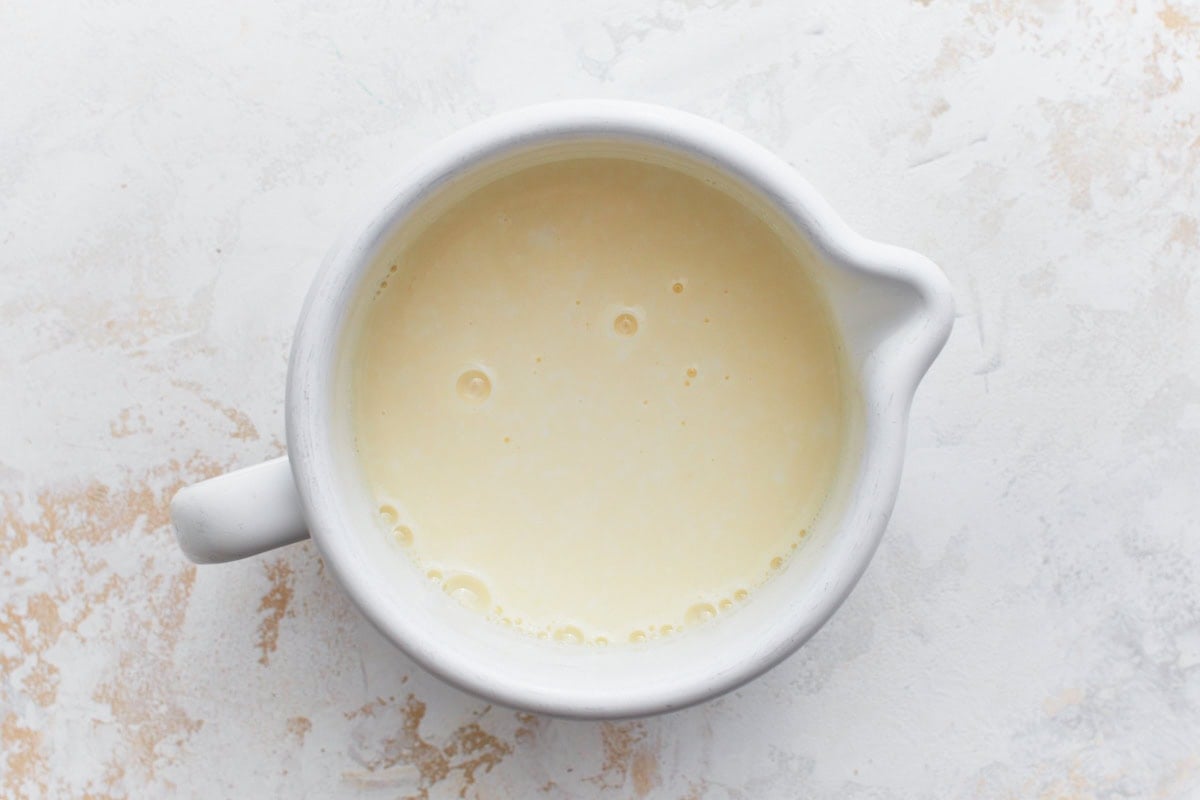 A white ceramic bowl filled with a creamy liquid mixture, potentially buttermilk and egg