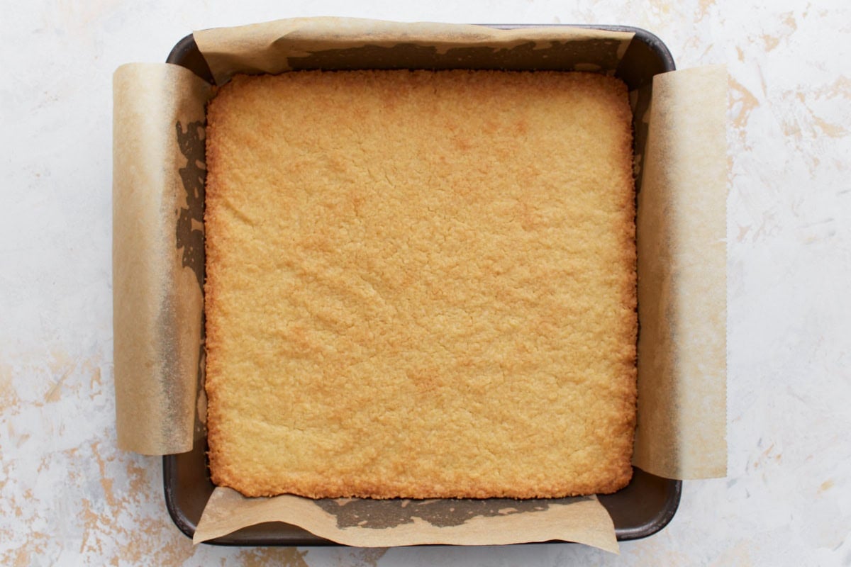 The baked gluten-free shortbread base, golden brown and evenly baked, in a parchment-lined pan.