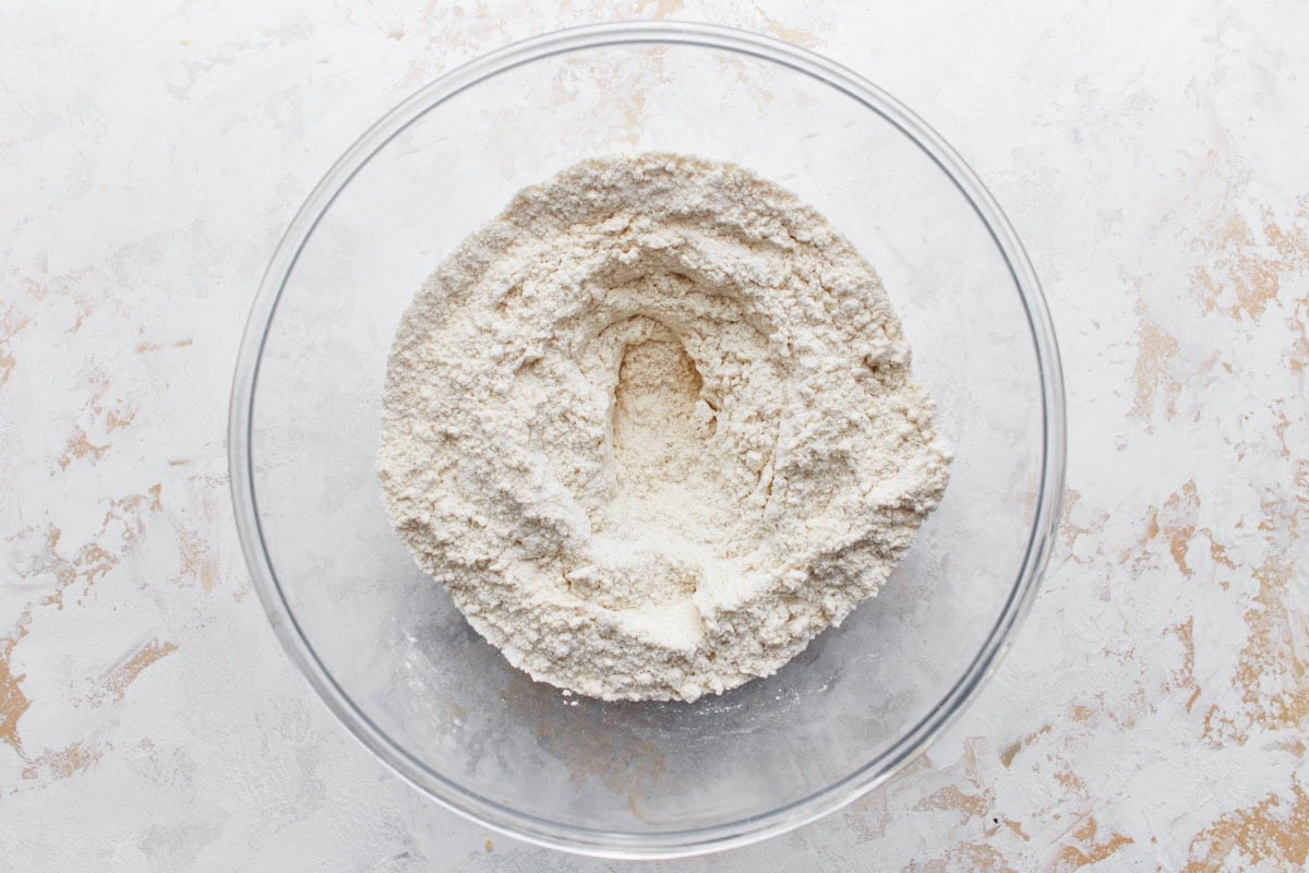 A mixing bowl containing gluten-free flour with a well in the center, ready for wet ingredients.