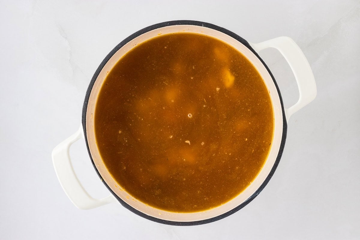 A pot of chicken broth with visible seasonings, ready to simmer and cook the soup.